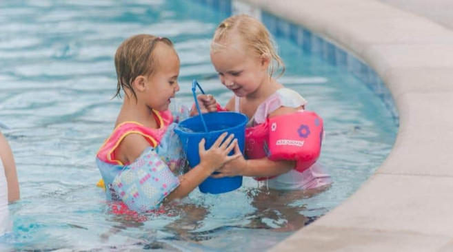 two children playing with a bucket in a swimming pool